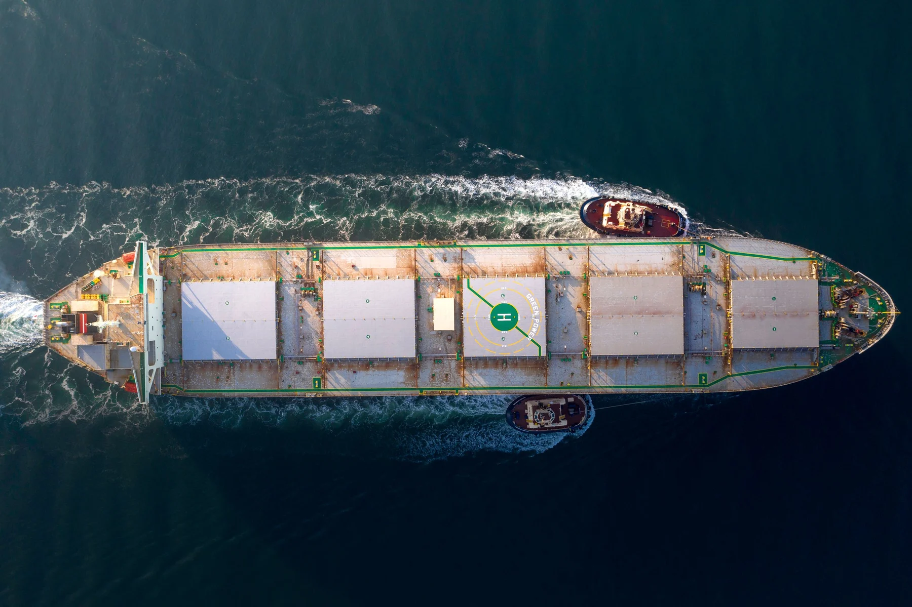 Overhead view of a cargo ship and tugboats moving through deep blue water